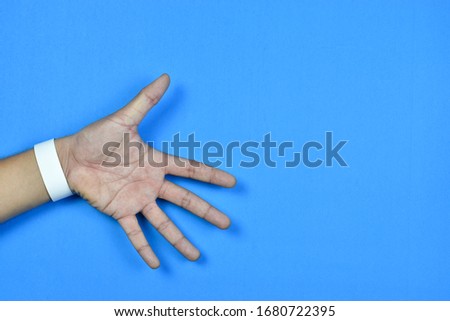 Top view of hand of showing with empty wristband on blue pastel on background view. Flat lay creative ideas on copy space.