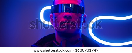panoramic shot of mixed race cyberpunk player in futuristic glasses near blue neon lighting Royalty-Free Stock Photo #1680731749