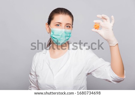 Doctor woman in a white coat, mask and gloves holds a mock virus in her hands. Studio photo on a white background.