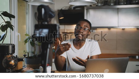 Happy young smart black blogger man filming new vlog video with professional camera in kitchen at home slow motion. Royalty-Free Stock Photo #1680737038