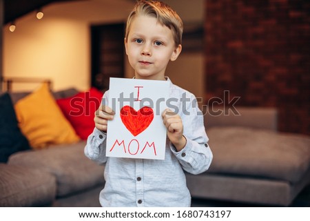 Happy mother's day! A handsome boy holding a postcard for his mother isolated on a blue background