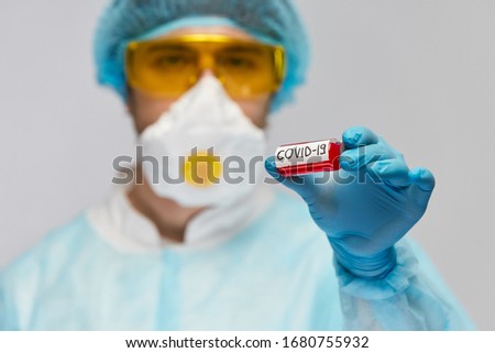 laboratory doctor in safety biohazard suit holding COVID-19 antivirus in arm with blue gloves