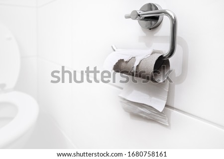 Out of stock, no more toilet paper. Last piece of paper on a roll in a clean and empty white bathroom. Panic, fear and world wide shopping crisis related to the outbreak of the COVID-19 coronavirus. Royalty-Free Stock Photo #1680758161