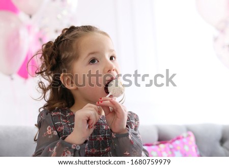 pretty curly girl in a gray flower dress eats candy on a stick with pleasure