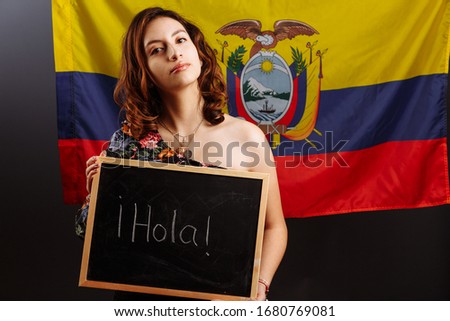 Portrait of young Latin American woman student holding a chalkboard with Hello word on her native language before the Ecuadorian flag