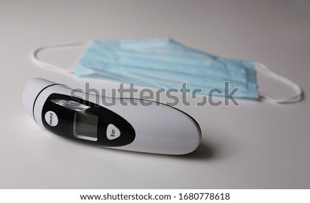 Contactless thermometer and medical mask on a white table