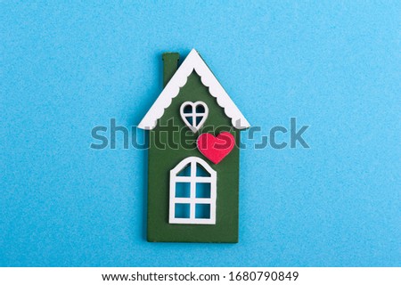 Green wooden house and heart on blue background with copy space. Safety or quarantine concept, home protection, real estate insurance, private property