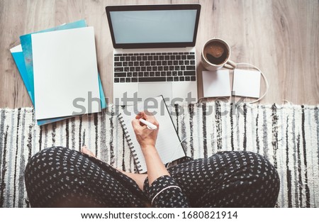  Businesswoman dressed pajamas writing day plan enjoying morning coffee on living room floor office with laptop, papers and other stuff top view shot.Distance work in worldwide quarantine time concept Royalty-Free Stock Photo #1680821914