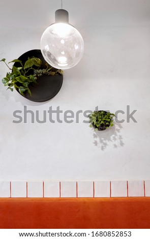 White wall with round pots with plants .White tiles with orange lines. Lines of orange sofa.