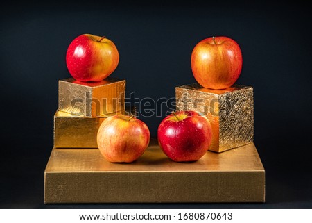 Red-yellow apples on geometric shapes on a dark background.