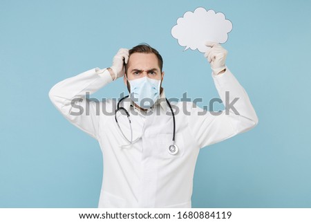 Preoccupied male doctor man in medical gown face mask gloves isolated on blue background. Epidemic pandemic coronavirus 2019-ncov sars covid-19 flu virus concept. Hold blank Say cloud speech bubble