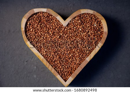 Buckwheat in a wooden plate in the shape of a heart isolated on background. Love for buckwheat porridge. Buckwheat groats, seeds. Useful gluten-free cereal. Close-up, top view.