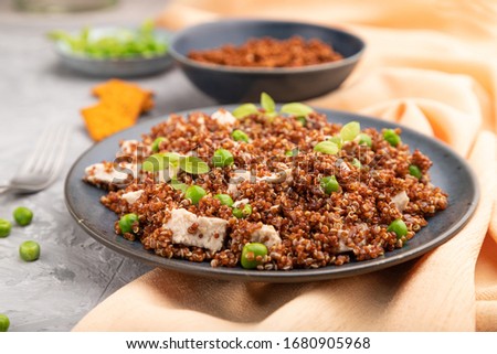 Quinoa porridge with green pea and chicken on ceramic plate on a gray concrete background and orange textile. Side view, close up, selective focus.