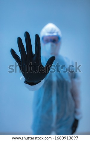 Medical doctor, scientist in full body suit for prevention from viruses and diseases holding a stop sign with hand - stop viral spreading.