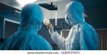 Medium shot of researchers wearing protective gear and examining coronavirus sample in virus laboratory Royalty-Free Stock Photo #1680929695