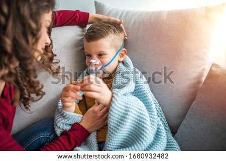 Mother helps her little boy to makes inhalation at home. Young woman with son doing inhalation with a nebulizer. Child, Ventilator, Breathing Exercise, Problems, Patient Royalty-Free Stock Photo #1680932482