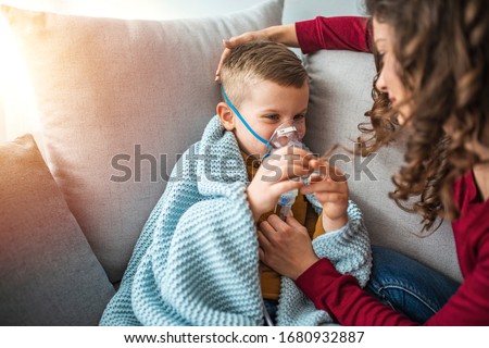 Mother helps her little boy to makes inhalation at home. Young woman with son doing inhalation with a nebulizer. Child, Ventilator, Breathing Exercise, Problems, Patient