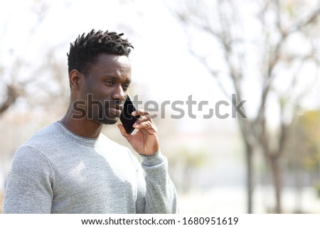 Serious black man calling on smart phone standing at the park Royalty-Free Stock Photo #1680951619