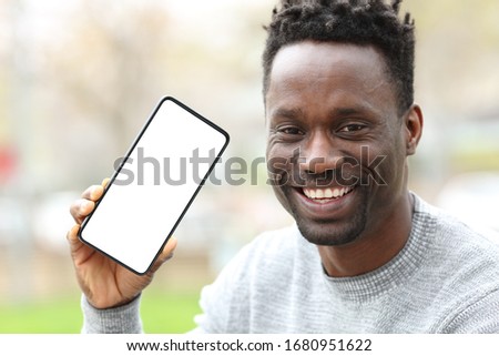 Front view portrait of a happy black man showing smart phone with blank screen in the park