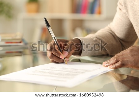 Close up of black man hands signing document on a desk at home Royalty-Free Stock Photo #1680952498