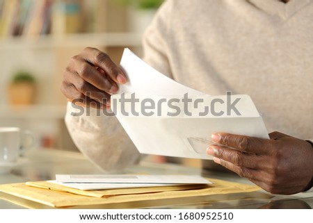 Close up of black man hands putting a letter inside an envelope on a desk at home Royalty-Free Stock Photo #1680952510