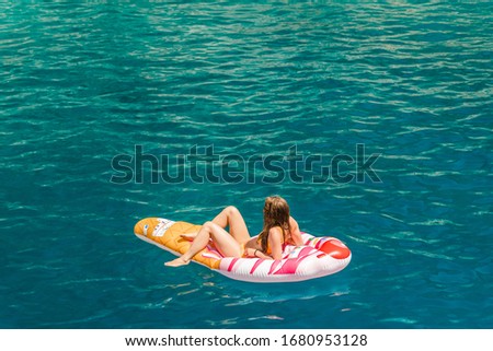 A girl in a bikini relaxes on an inflatable ice cream cone floatie on bright blue mediterranean water while on vacation in the summer.
