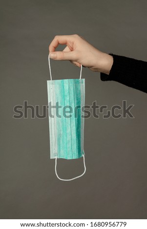 Girl is holding a three-layer disposable medical mask for respiratory protection. Photo on a grey background