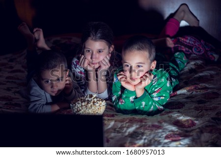 Children looking at laptop with cartoons showing before sleeping in bed. Three children in bed watching a movie on a laptop. toned