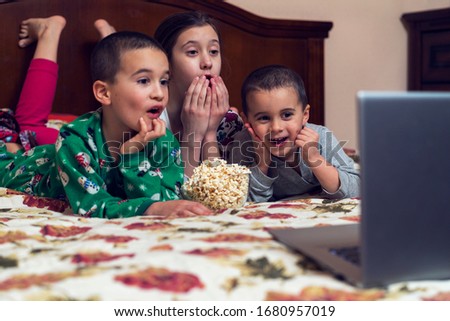 Children looking at laptop with cartoons showing before sleeping in bed. Three children in bed watching a movie on a laptop