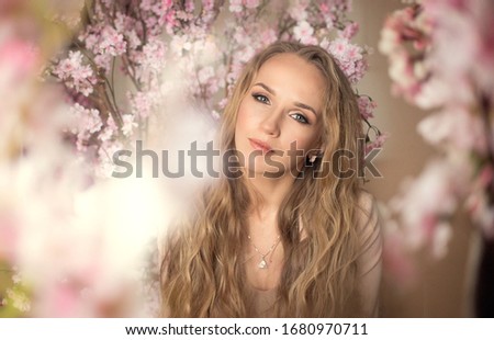 
Very beautiful young woman with long blond hair and blue eyes. Photos on a background of blooming cherry. Image with selective focus and toning.