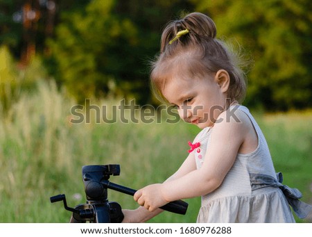 A 2-year-old girl plays on the street with a tripod for cameras