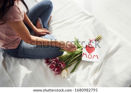 Top view of woman that sits on bed with bouquet of flowers and post card with heart pictures on it.