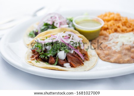 A view of two tacos al pastor with a side of beans and rice. Royalty-Free Stock Photo #1681027009