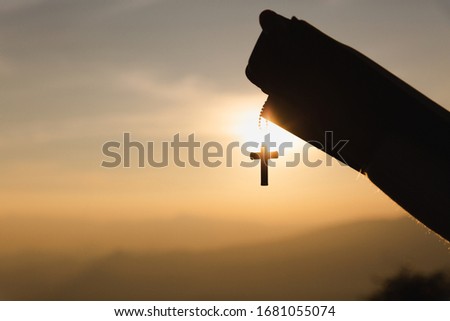 human hands praying to the GOD while holding a crucifix symbol with bright sunbeam. 
