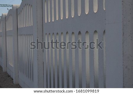 Cement and stone hedges. The device is a solid white fence made of concrete slab with vertical repeating slots. It is used at railway stations, public and industrial facilities.