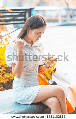 orange tone of a woman in white dress using smart phone for shopping online 