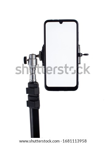 Smartphone mounted on a black tripod in a vertical position on a light isolated background tilted to the right. Royalty-Free Stock Photo #1681113958