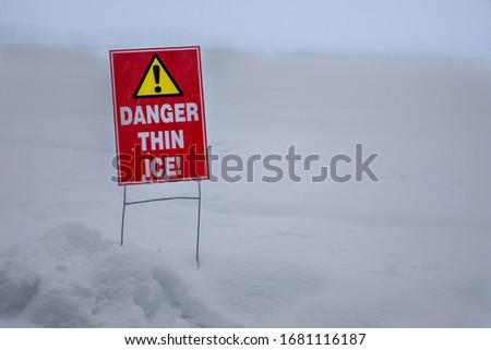 Sign talking about the dangers of thin ice near a frozen lake