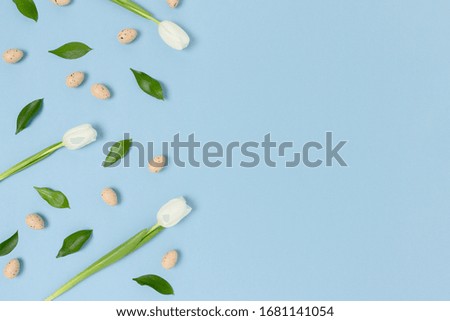 Pattern frame made of flowers and easter eggs on a blue pastel background. Holiday creative concept with copy space.