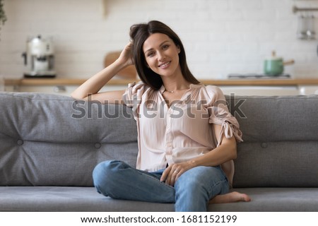 Portrait of smiling young woman sit relax on comfortable couch enjoy weekend in cozy home, happy millennial girl rest on sofa in living room looking at camera posing, renting, ownership concept