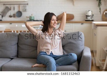 Smiling young woman sit rest on cozy couch at home look in distance dreaming, happy millennial girl relax on comfortable sofa in living room thinking pondering enjoying leisure weekend indoors Royalty-Free Stock Photo #1681152463