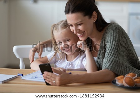 Happy mum and little daughter make self-portrait picture use cellphone together, smiling young mother and sweet small girl child look at camera taking posing for selfie, have video call on smartphone