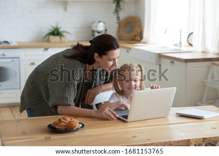 Loving young mum and little preschooler daughter sit at kitchen table using laptop together, caring mother help small girl child teaching learning online on computer, kids and technology concept Royalty-Free Stock Photo #1681153765