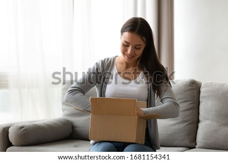 Happy young woman sit on couch in living room unpack cardboard box buying goods on Internet, smiling excited millennial girl open carton parcel order, shopping online, good delivery concept Royalty-Free Stock Photo #1681154341