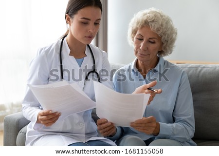 Young woman doctor visit senior old lady patient at home explain medical documents insurance, attentive female give consultation close sign healthcare agreement with elderly grandmother at home