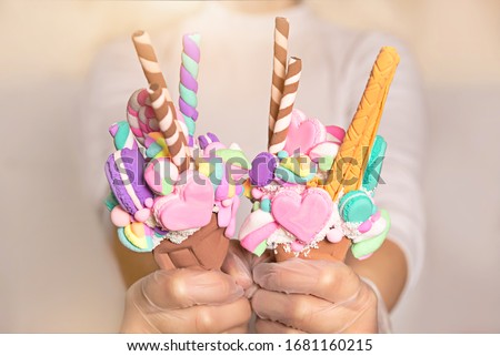Artificial dessert made of polymer clay and light plasticine. Waffle Cup with sweets, marshmallows, macaroni, in the hands of latex gloves.
