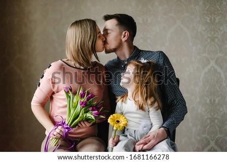 Happy mother's day! Daughter with dad congratulate mom and give her flowers tulips. Mum, father kissing and hugging. Family holiday and togetherness. International Women's Day.