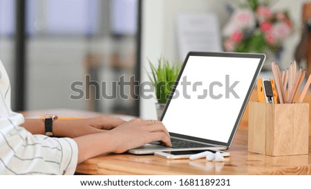 Cropped image of beautiful woman working as secretary typing on computer laptop while sitting at the wooden working desk over comfortable workplace as background.