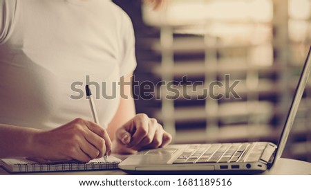 close up of Young businesswoman sitting in modern office with laptop and taking notes in notebook