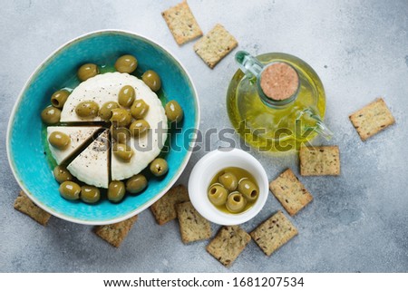 Soft cheese with green olives, olive oil, black pepper and crackers. Top view on a light-blue stone background